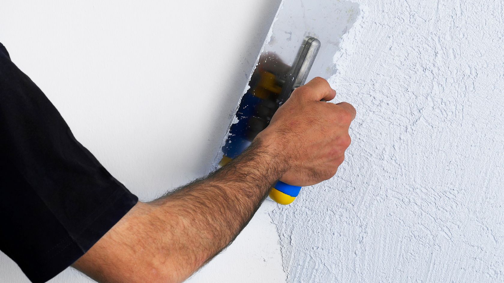 a person's arm using a scraper to apply spcakle to a wall